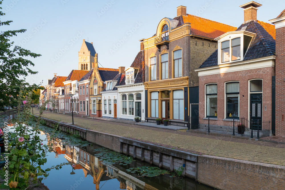 Colorful traditional old houses along the canal and in the background the tower of the martini church in the picturesque town of Bolsward in Friesland, the Netherlands.