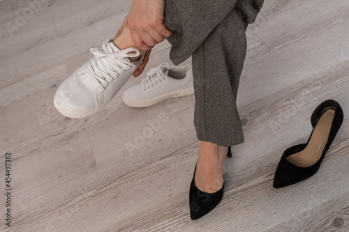 Close-up business woman takes off her shoes puts on white leather sneakers.