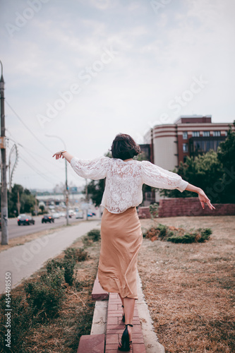 A happy girl on the river bank, standing on the bridge, smiling, a girl walks on the bridge by the river. Freedom. The wind is blowing the girl's hair.