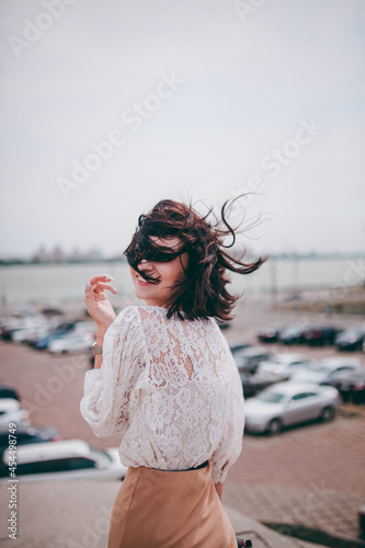 A happy girl on the river bank, standing on the bridge, smiling, a girl walks on the bridge by the river. Freedom. The wind is blowing the girl's hair.