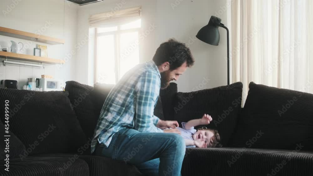A happy father playing with his baby sitting on the sofa at home