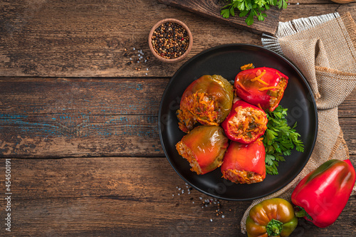 Red and green bell peppers stuffed with meat and rice in a black plate on a wooden background. Stewed pepper with meat and vegetables.