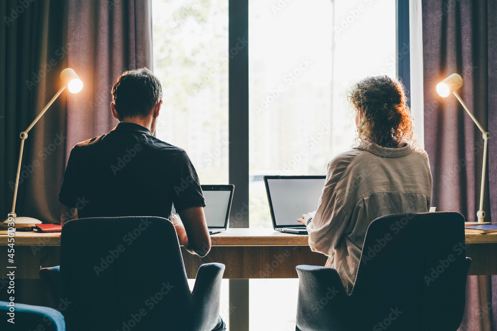 Family of middle aged man and woman at work together on project with contemporary laptops at long counter near large window at home - obrazy, fototapety, plakaty 