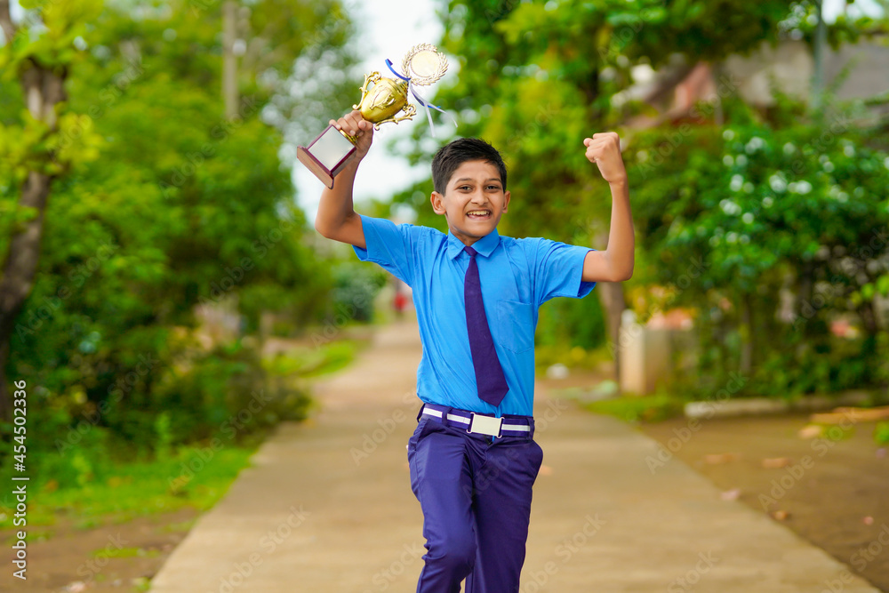 Obraz premium Clever schoolboy raising his trophy as a winner in school competition.