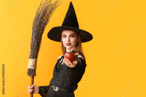 Young witch with apple on color background