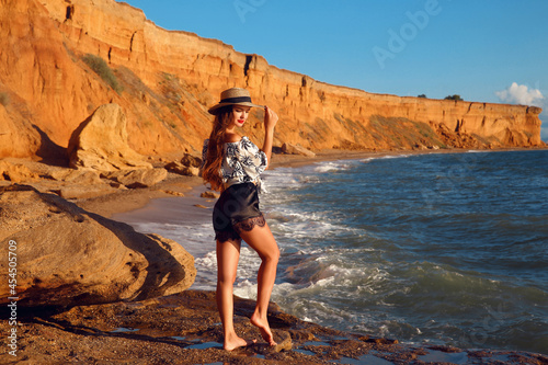 Summer photo of Sexy brunette girl with hat in fashion casual outfit enjpying on the beach at sunset. Freedom summertime vacation concept. Enjoyment.