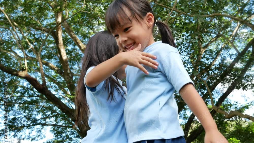 Two sibling little girls laughing and hugging each other on warm and sunny summer day in the garden. Children playing in the playground. Two sibling little girls laughing and hugging each other on warm and sunny summer day in the garden. Children playing in the playground.