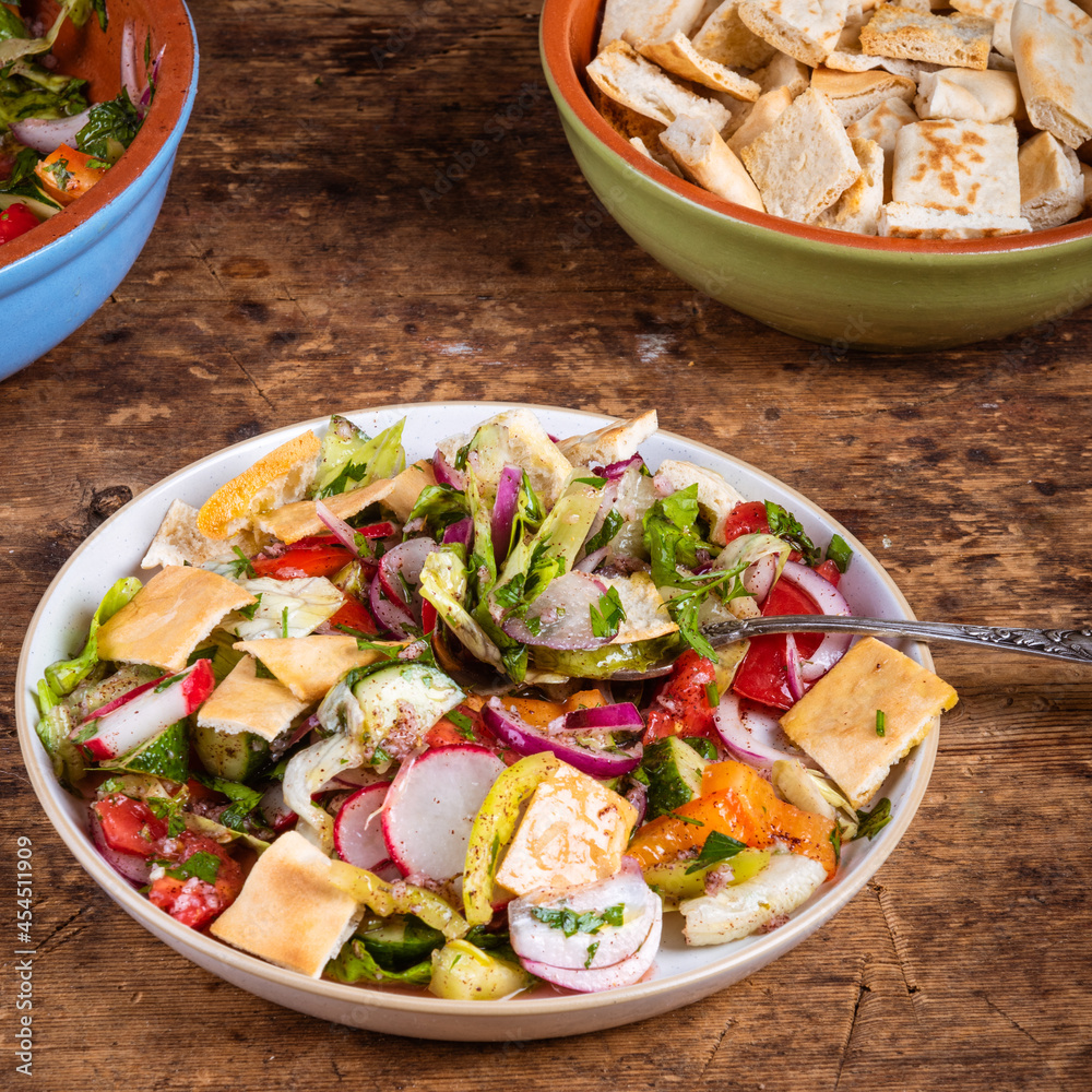 Arabic vegetarian salad Fattoush of tomato, onion, cucumber and pepper with pita croutons in a plate on the table, close-up with bowls of salad and croutons