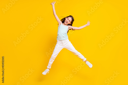Full body photo of happy positive pretty little girl good mood raise hands jump isolated on yellow color background