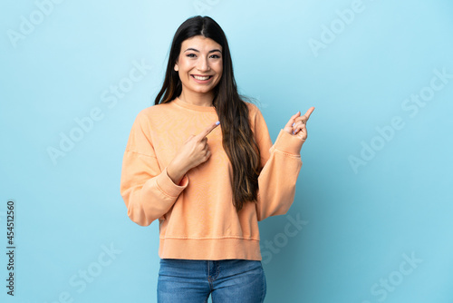 Valokuva Young brunette girl over isolated blue background frightened and pointing to the