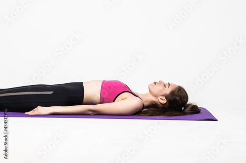 Sporty beautiful young woman in white sportswear lying with closed eyes on mat in Shavasana isolated on white background