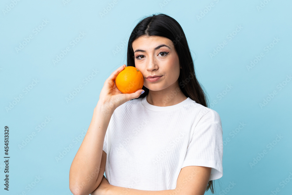 Young brunette girl over isolated blue background holding an orange Young brunette girl over isolated blue background holding an orange