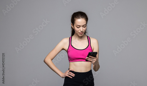 Portrait of young sport woman waring sport bra and leggings use smartphone over white background. Female holding phone and chat.