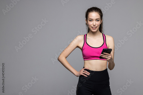 Portrait of a happy fitness woman standing and using mobile phone over white background