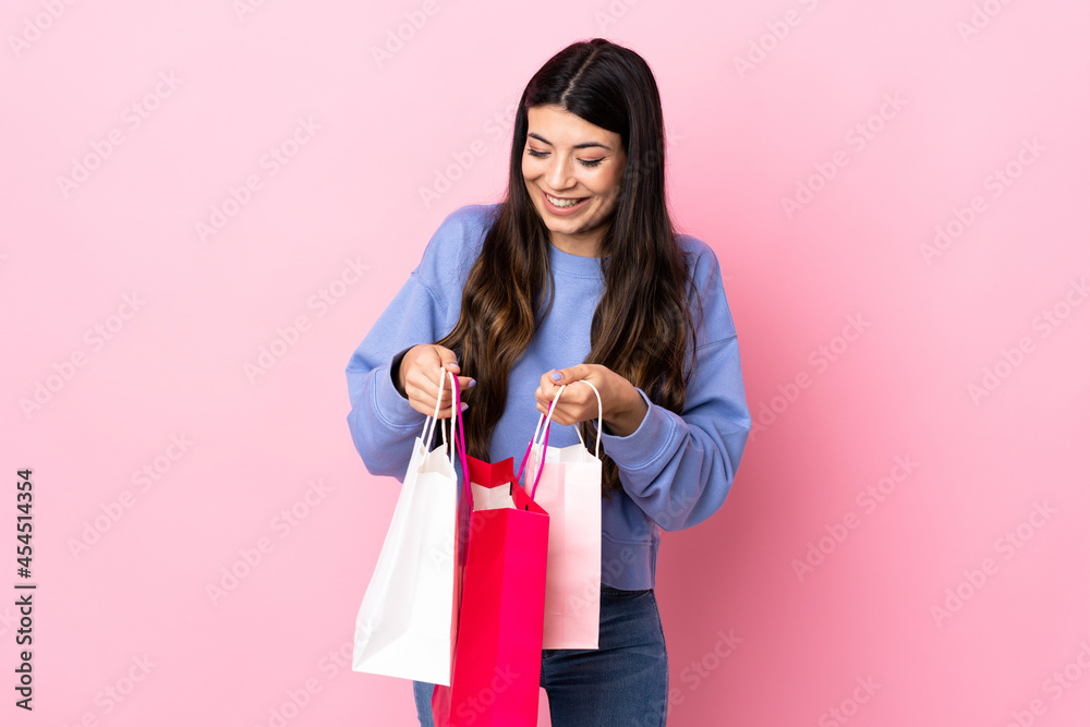 Young brunette girl over isolated pink background holding shopping bags and looking inside it