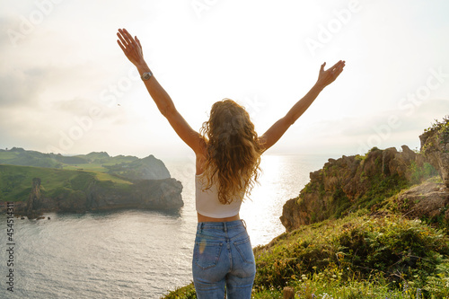 Unrecognizable woman in a cliff. Horizontal view of caucasian woman from behind breathing with arms wide open