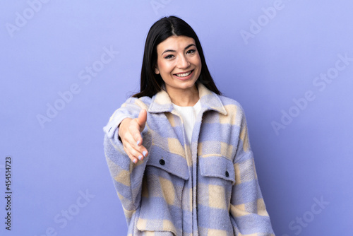 Young brunette woman over isolated purple background shaking hands for closing a good deal © luismolinero