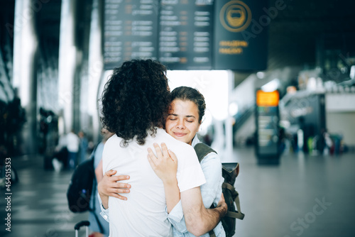 Young family couple at the airport departure area saying goodbye or hello, embracing each other with smile. Arrival and reunion awaiting after travel