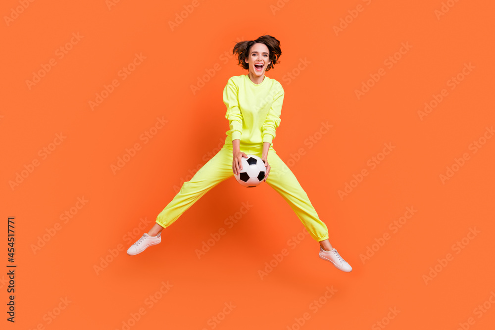 Full length body size view of attractive cheery girl jumping playing soccer match isolated over bright orange color background