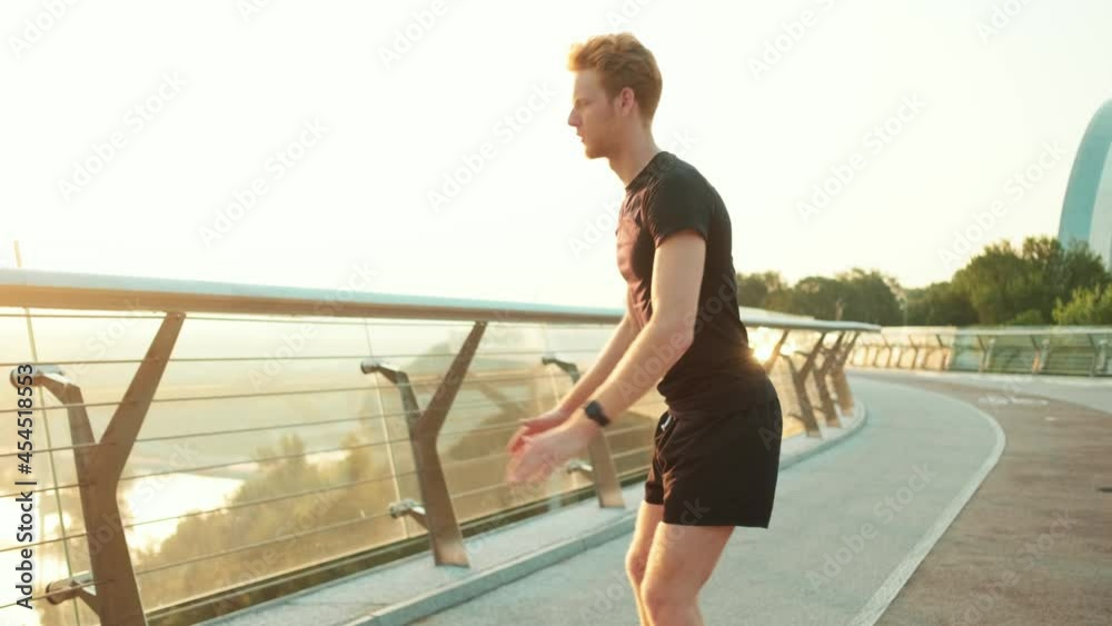 A sportsman training while doing squats outdoors on the bridge A sportsman training while doing squats outdoors on the bridge