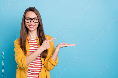 Photo of young woman happy positive smile point finger product promo advert choice sale isolated over blue color background photo