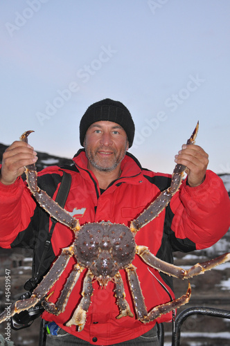 Portrait of happy fisherman in red jacket with caught huge red king crab in Barents Sea