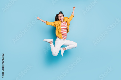 Full size photo of young woman happy positive smile celebrate victory lucky success jump isolated over blue color background