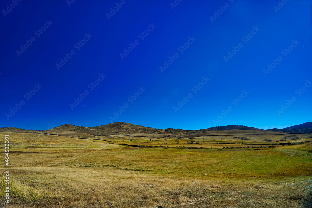 A dried out meadow in autumn. The background is blue sky and hills.