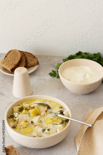 Chicken breast and sorrel soup with potatoes and sour cream, a bowl of soup on the table, bread and parsley