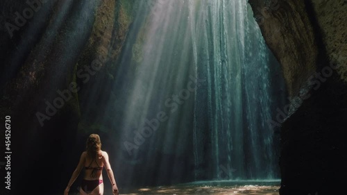 happy woman dancing in waterfall cave wearing bikini having fun enjoying freedom with arms raised feeling carefree tropical vacation 4k