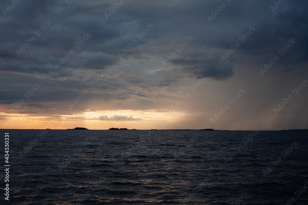 Sunset over the sea, with waves, stormy clouds and rain.