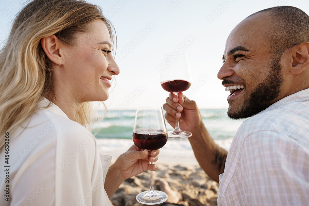 Portrait of a young couple sitting on the beach and drinking wine Portrait of a young couple sitting on the beach and drinking wine