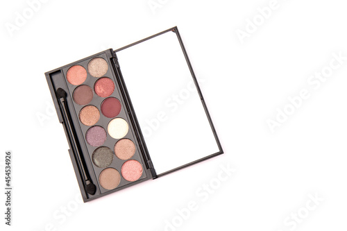 Eyeshadow palette. Black plastic case with twelve powder matte, glitter paint sample in purple, pink, brown, vanilla colors and brush. Top view makeup box isolated on white background