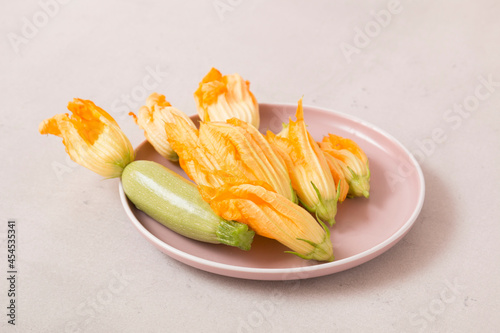 Zucchini and zucchini flowers in a plate on white marble background
