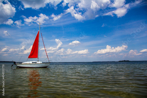 Small yacht with a red sail on a beautiful lake