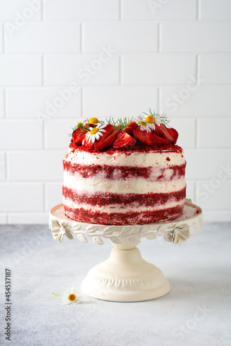 Red velvet cake with strawberry, whipped cream and bouquet of daisies on white board on gray background. Valentines Day, Wedding dessert or Birthday party. Bakery, confectionery concept. Copy space.