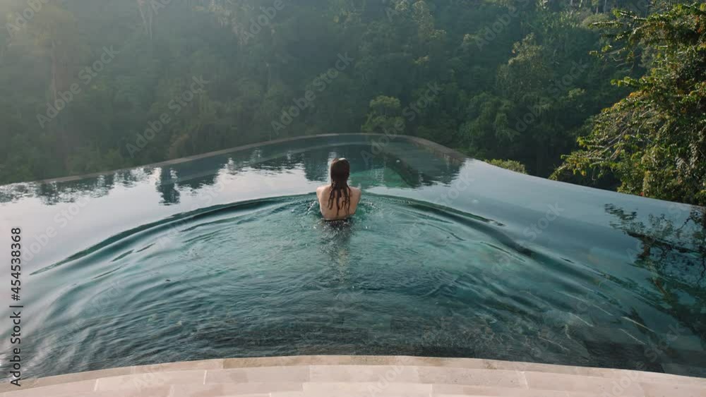 sexy woman swimming in infinity pool enjoying luxury lifestyle on exotic summer vacation at hotel spa with view of tropical jungle