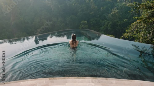 sexy woman swimming in infinity pool enjoying luxury lifestyle on exotic summer vacation at hotel spa with view of tropical jungle photo