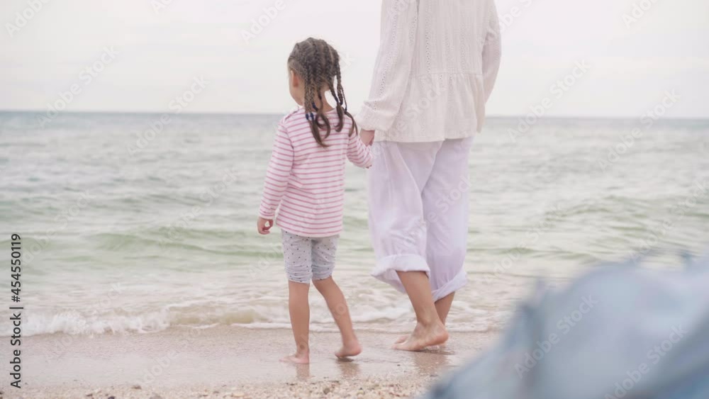 Mother With Little Daughter Walking Along the Sea Happy Family on the Beach Mother holds hand little child walking along the seashore. Traveling Summer Vacation Concept Mother With Little Daughter Walking Along the Sea Happy Family on the Beach Mother holds hand little child walking along the seashore. Traveling Summer Vacation Concept