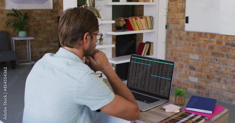 Caucasian man sitting at desk watching coding data processing on laptop screen Caucasian man sitting at desk watching coding data processing on laptop screen