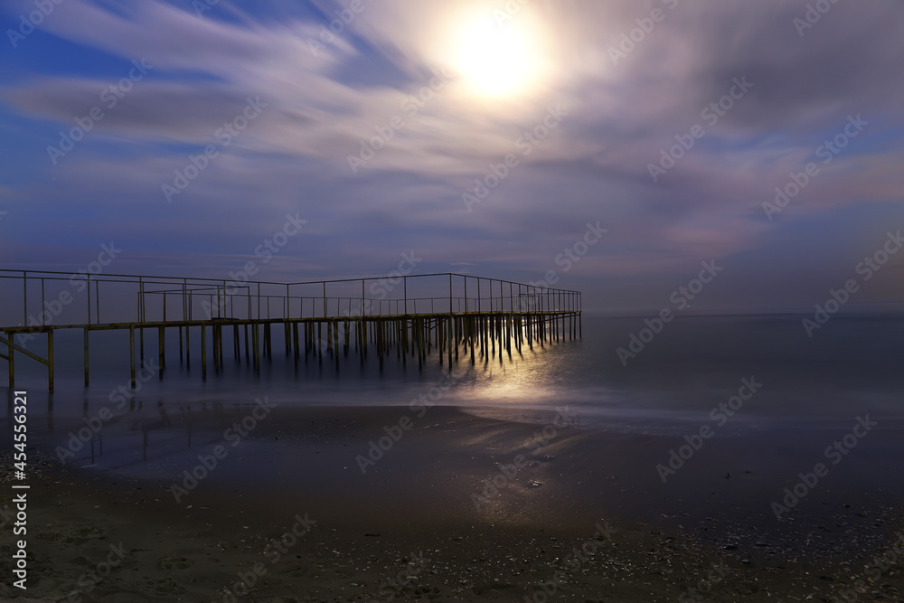 Night photo. Old ruined pier and sea with a full moon.