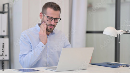 Middle Aged Man with Toothache Drinking Water while using Laptop 