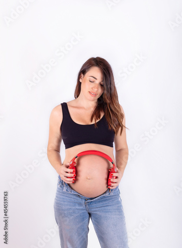 A pregnant woman holding red headphones close to her stomach, isolated on a white background.