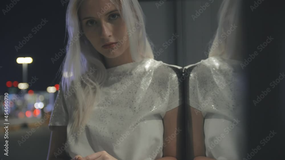 Slow motion pretty woman stands leaning on a glass wall at night in bright light reflecting in glass Slow motion pretty woman stands leaning on a glass wall at night in bright light reflecting in glass