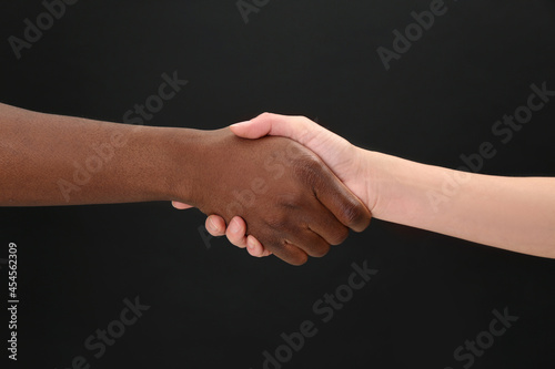 Woman and African American man shaking hands on black background, closeup