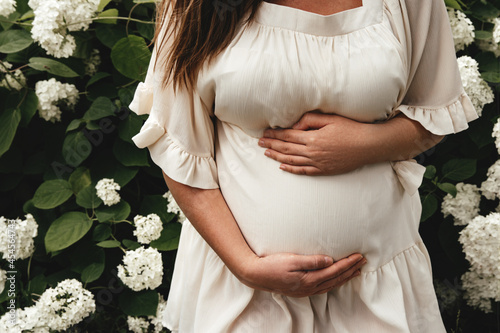 A pregnant woman in a white dress holds her hands on her stomach