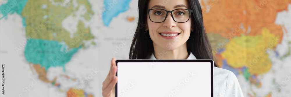 Woman with glasses holding empty digital tablet in hands against background of geographic map of world Woman with glasses holding empty digital tablet in hands against background of geographic map of world