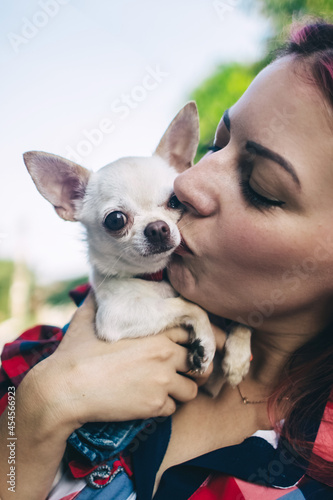 The girl holds a mini chihuahua in her arms. Kissing your pet. The dog and the owner are dressed in the same color. Clothes for animals. Love and care for four-legged pets.