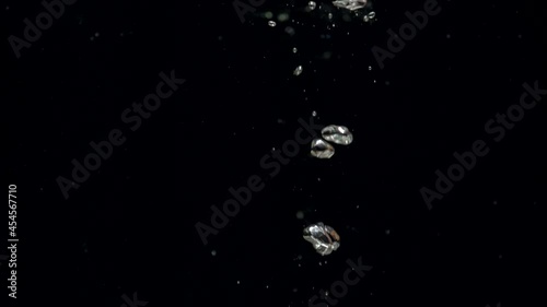 Slow motion air bubbles in water rising up to the surface on isolated black background. Slowmotion air bubbles floating under transparent water bubbles in aquarium