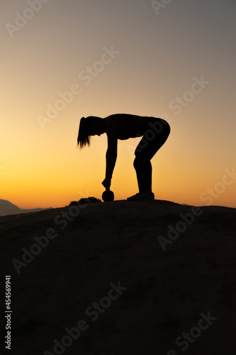Silueta de chica haciendo ejercicio de espalda, con kettlebell, en la hora del atardecer al aire libre en la montaña. © Ezequiel Martínez